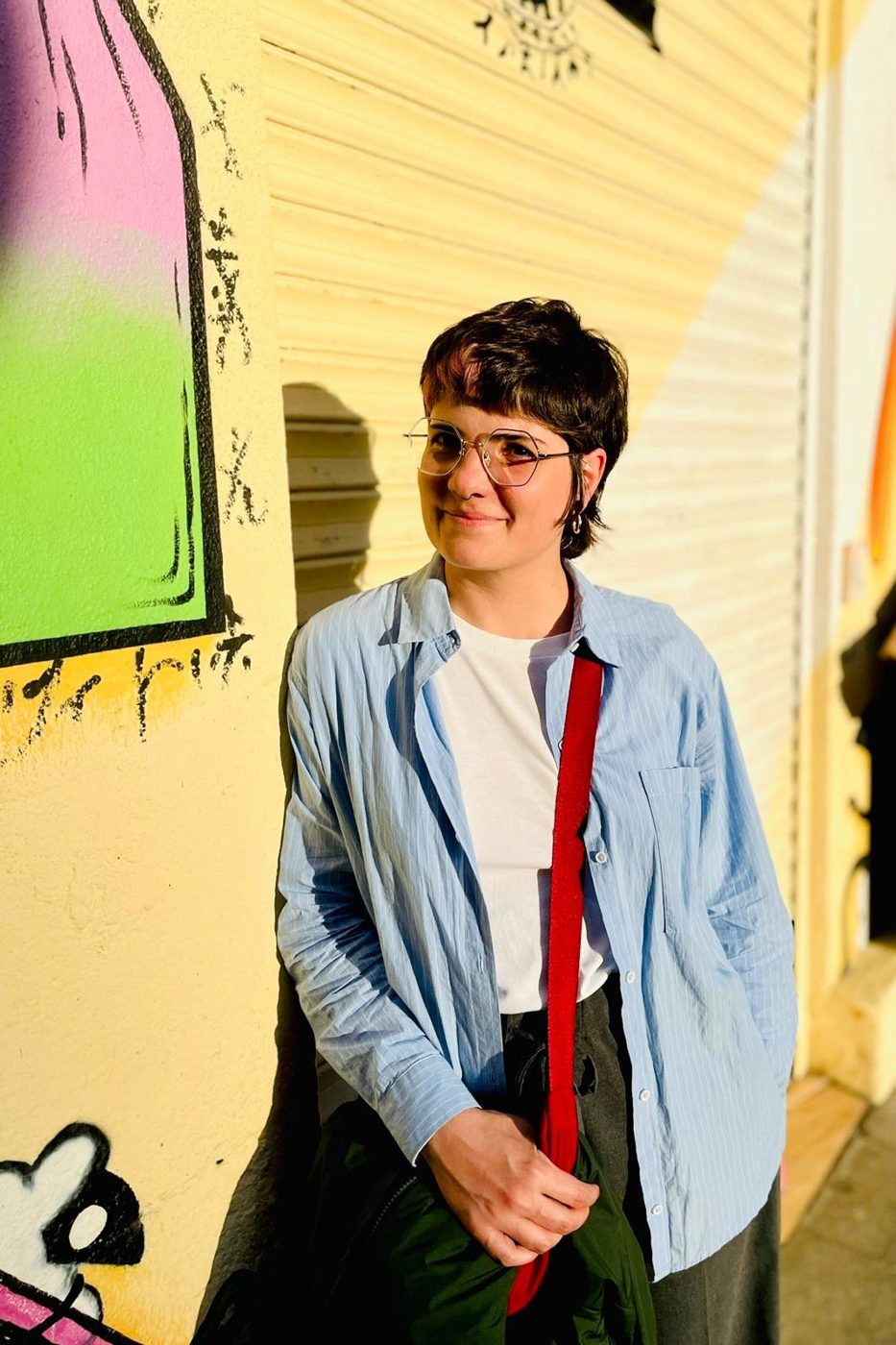 Érica Santillán apoyada en una pared pintada con grafitis, sonriendo